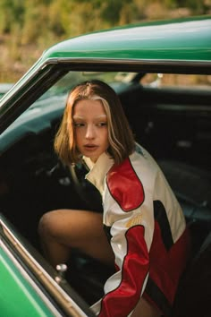 a woman sitting in the driver's seat of a green car with her hand on the door handle