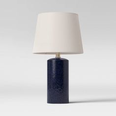 a blue table lamp with a white shade on the top and bottom, in front of a gray background