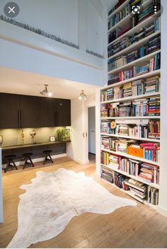 a book shelf filled with lots of books next to a white cow skin rug on top of a hard wood floor