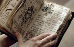 a person holding an old book in their hands with writing on the pages and symbols