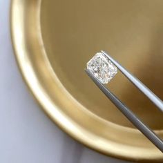 a close up of a diamond in a gold bowl with two tongs on it