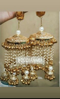 two gold and white chandeliers with pearls hanging from the ceiling, one is being held by a hand