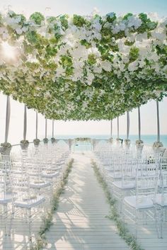 an outdoor wedding setup with white chairs and greenery on the aisle, overlooking the ocean