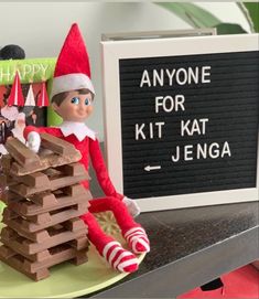 an elf is sitting on top of a stack of wooden blocks next to a sign that says anyone for kit kat jenga