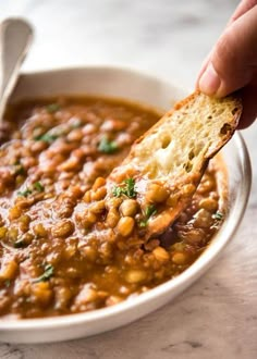 a hand holding a piece of bread over a bowl of beans