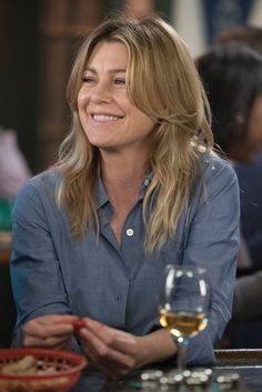 a woman sitting at a table with a glass of wine in front of her smiling