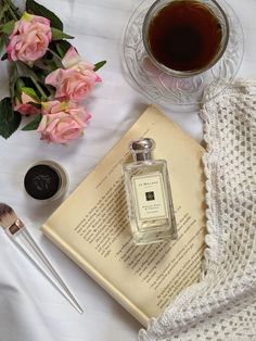 an open book next to a cup of tea and some flowers on a white table