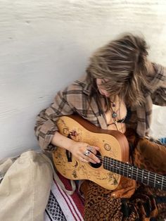 a woman sitting on the floor playing a guitar with her hair blowing in the wind