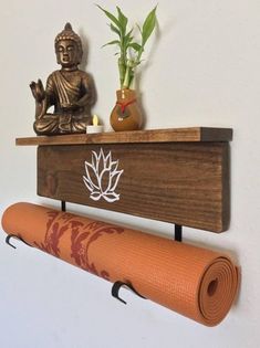 a buddha statue sitting on top of a wooden shelf next to a yoga mat and potted plant