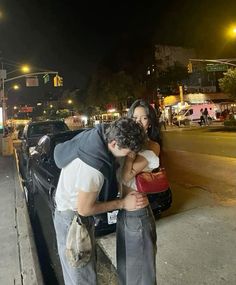 a man kissing a woman on the cheek in front of a black car at night