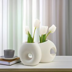 white flowers are in a vase next to a book and coffee cup on a table