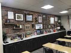 an empty classroom with desks and pictures hanging on the brick wall behind the desk