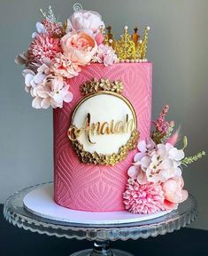 a pink cake decorated with flowers and a crown on top that says anana in gold lettering