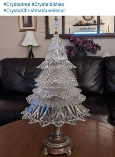 a glass christmas tree sitting on top of a wooden table next to a black couch