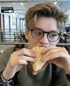 a young man wearing glasses eating a sandwich