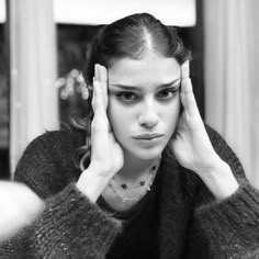 a woman holding her hands to her head while looking at the mirror in black and white