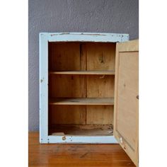 an old wooden cabinet with two shelves and one door open on a wood floor in front of a gray wall