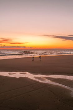 two people walking on the beach at sunset