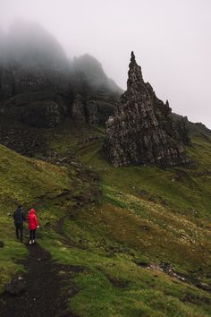 two people walking up a trail in the mountains on a foggy, cloudy day