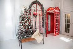 a red phone booth next to a christmas tree in a room with white walls and floors