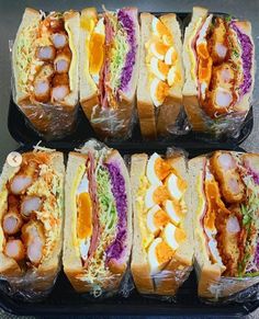 several sub sandwiches are lined up in plastic containers