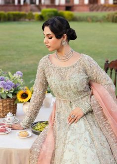 a woman sitting at a table with food and flowers in front of her on the grass