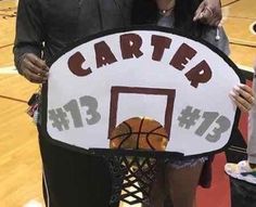 a man and woman holding up a sign for a basketball game