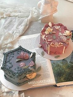 two cakes sitting on top of a table next to an open book