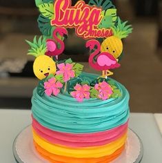 there is a colorful cake decorated with flamingos and pineapples on the top