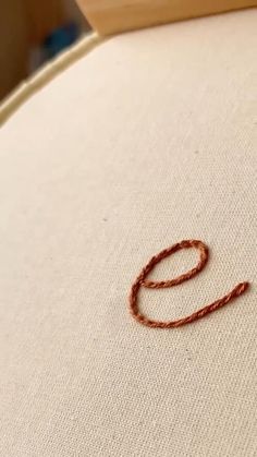 an orange thread is laying on top of a white cloth with the letter o in it