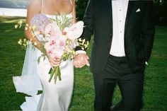 the bride and groom are walking together in their wedding attire, holding hands with each other