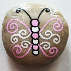 a painted rock with a butterfly on it's back and pink, white, and black designs