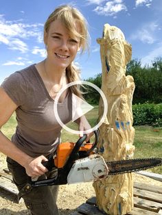 a woman is holding a chainsaw in front of a carved wooden bear and tree