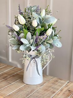 a white watering can filled with flowers and greenery