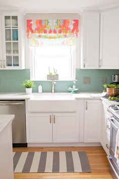 a kitchen with white cabinets and green backsplash, window above the stove top