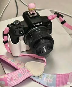 a camera with a pink strap around it's neck sitting on top of a table