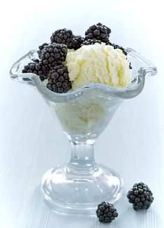 an ice cream sundae with blackberries in a glass bowl on a white background