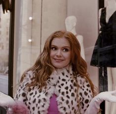 a woman standing in front of a store window with white gloves on her hands and wearing a leopard print coat