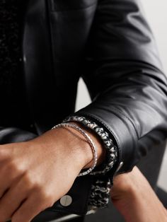 a person wearing a black leather jacket and bracelets with their hands on the wrist