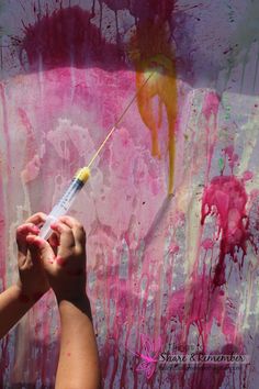 a child's hand holding a paintbrush in front of pink and yellow art