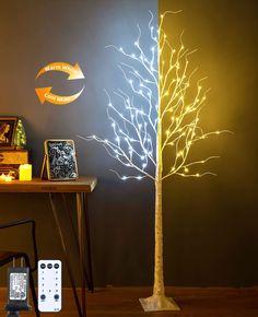 a lighted tree next to a table with a remote control and other items on it