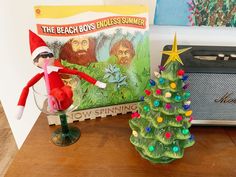 an elf is sitting next to the beach boys christmas tree and other holiday decor items