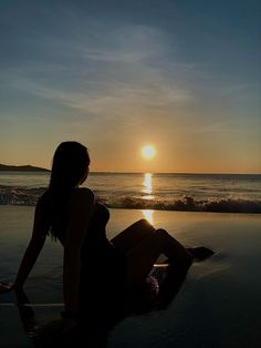 a woman sitting on the beach at sunset