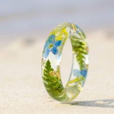 a close up of a ring on the sand with trees and flowers painted on it