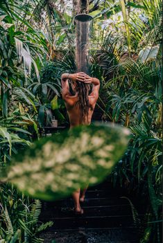 a naked woman walking up some stairs in the jungle with lots of greenery on either side