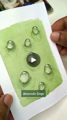 someone holding up a card with watercolor drops on it and the video is in front of them