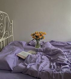 a white iron bed with purple sheets and flowers in a vase on the end table