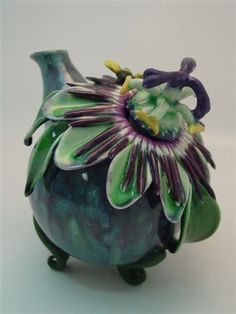 a green vase with purple and yellow flowers in it's center, on a white surface