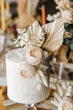 a white wedding cake decorated with flowers and feathers on top of a table in front of candles