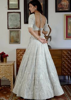 a woman in a white dress standing next to a wall with pictures on it and looking back